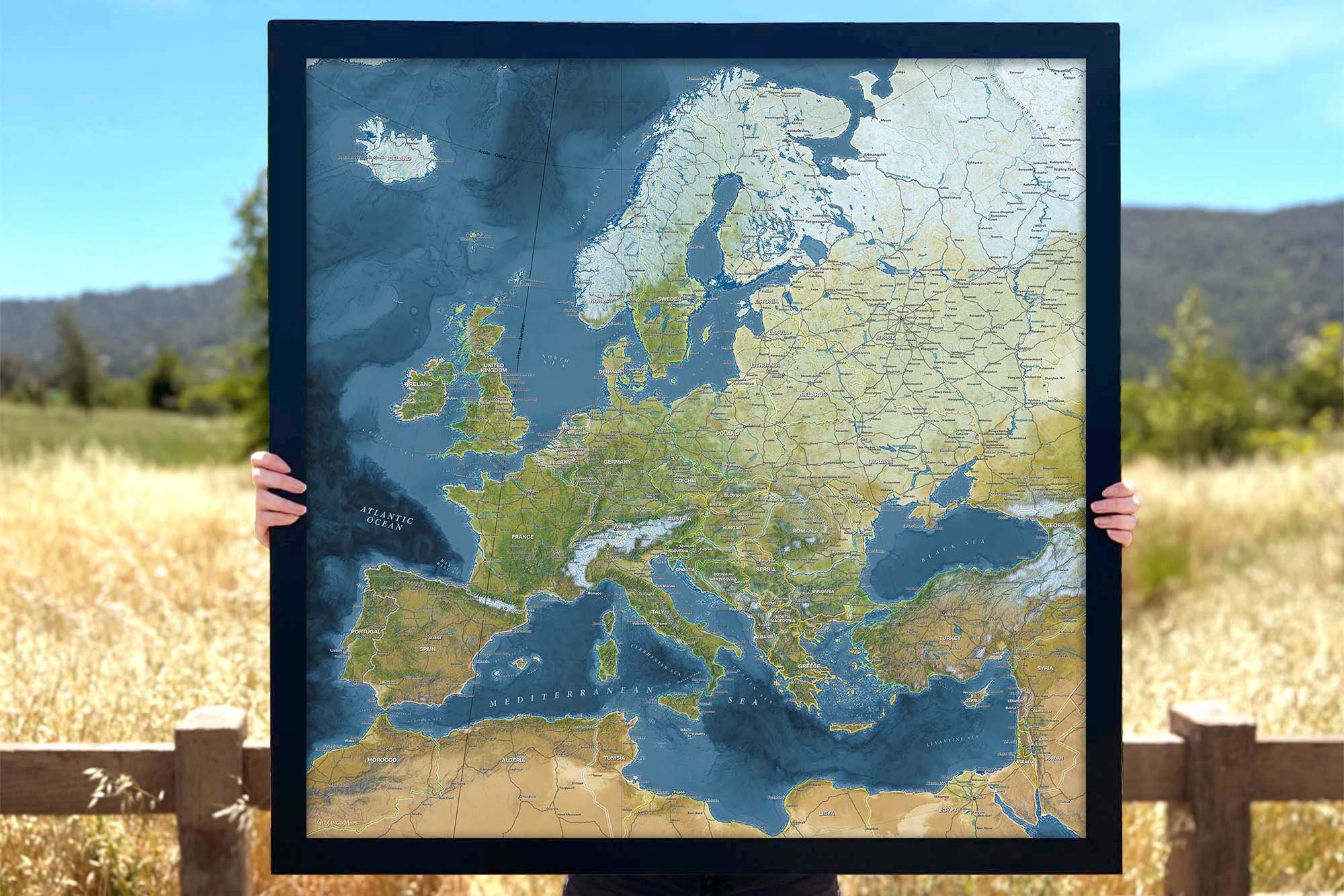 Person holding a push pin map of europe in a black frame