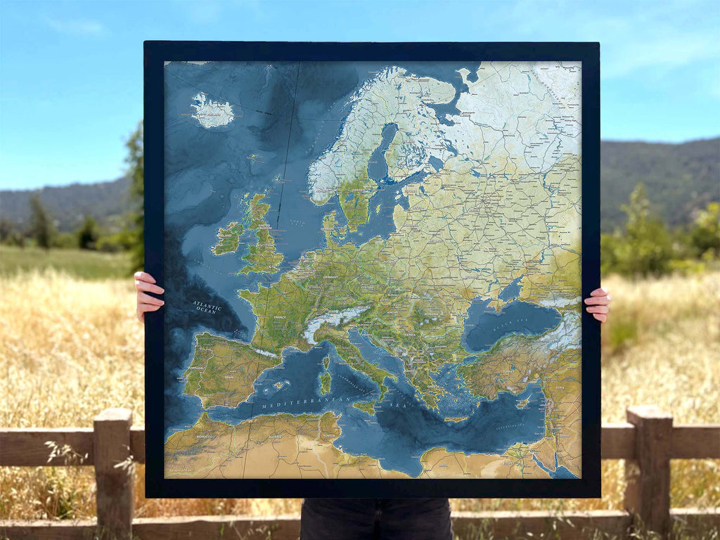 Person holding a push pin map of europe in a black frame